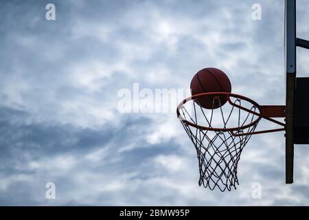 Dunkle Silhouette der Straße Basketball fällt in den Reifen an einem bewölkten Tag. Nahaufnahme eines Balls über dem Netz. Konzept des Erfolgs, Scoring po Stockfoto