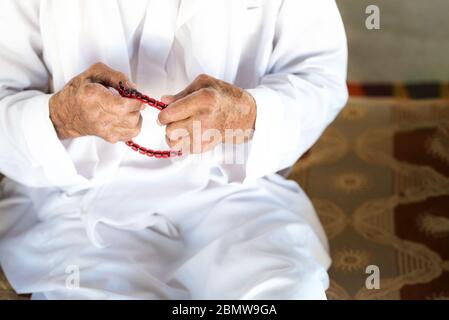 Arabischer Beduinenmann in traditioneller weißer Ferienkleidung. Nahaufnahme der betenden Hände eines alten Mannes, der den muslimischen Rosenkranz hält. Ramadhan Kareem Konzept. Stockfoto