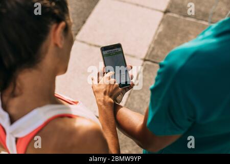 Nahaufnahme von zwei Fitnessleuten, die die Zusammenfassung ihres Laufs auf dem Mobiltelefon überprüfen. Mann und Frau Läufer mit einer Fitness-App auf ihrem Smartphone. Stockfoto