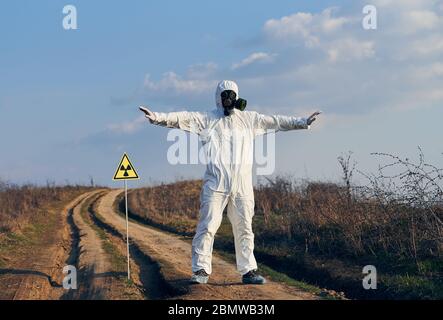 Volle Länge des männlichen Wissenschaftlers auf der Straße in der Nähe des gelben Dreiecks mit ionisierenden Strahlung Warnzeichen und Verbreitung Arme zu Seiten. Wissenschaftler tragen Schutzanzug, Gasmaske. Stockfoto