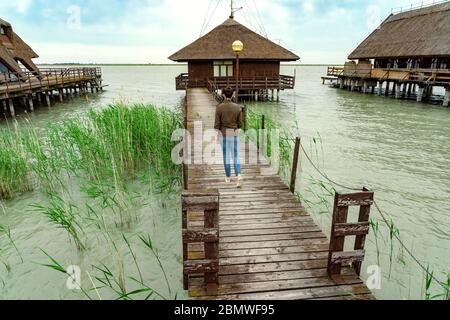 Ruhige Natur am See Fertő in Ungarn mit Holzsteg Bungalows Hütten auf dem See und Stroh im Wasser mit einer touristischen Frau zu Fuß auf dem Stockfoto