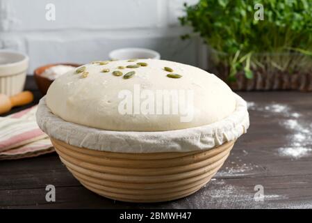 Frisch gekochter Hefeteig in einem Korb zum Backen mit Kürbiskernen für die Herstellung von frischen Naturkuchen und Brot ein dunkler Holzhintergrund, Kopie Stockfoto