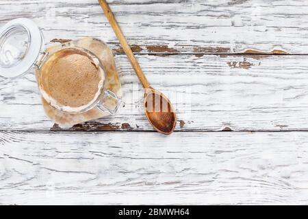 Aktive Vollkornsauerteigstarter mit Holzlöffel über einem weißen rustikalen Holztisch/Hintergrund mit freiem Platz für Text Bild von oben Stockfoto
