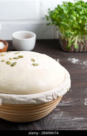 Frisch gekochter Hefeteig in einem Korb zum Backen mit Kürbiskernen für die Herstellung von frischen Naturkuchen und Brot ein dunkler Holzhintergrund, Kopie Stockfoto