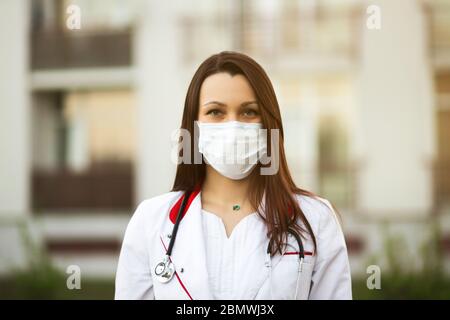 Online-Webinar oder Konferenzkonzept: Junge Ärztin in chirurgischer Maske und Ohrstöpsel im Freien Stockfoto