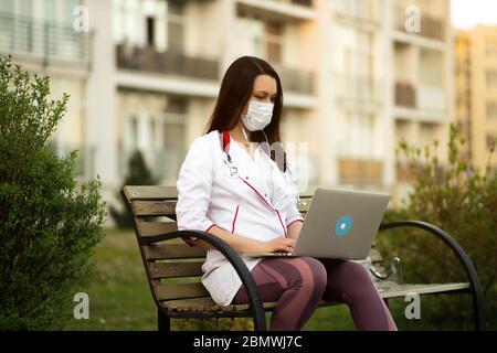 Junge Ärztin in chirurgischen Maske verwendet Laptop im Freien Stockfoto