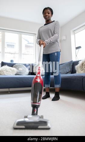 Teenage Girl Helfend Out With Chores At Home Vacuuming Carpet In Lounge With Cordless Cleaner Stockfoto