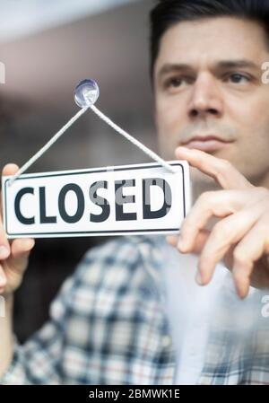 Männlich Small Business Owner Mit Ernsthaften Ausdruck Setzen Bis Closed Sign Während Der Rezession Oder Gesundheit Pandemie Stockfoto