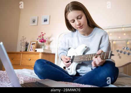 Teenager-Mädchen Sitzen Auf Bett Lernen, E-Gitarre Mit Online-Lektion Auf Laptop-Computer Zu Spielen Stockfoto