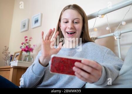 Lächelndes Teenage Girl Im Schlafzimmer Mit Freunden Über Soziale Medien Über Handy Sprechen Stockfoto