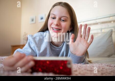 Lächelndes Teenage Girl Im Schlafzimmer Mit Freunden Über Soziale Medien Über Handy Sprechen Stockfoto