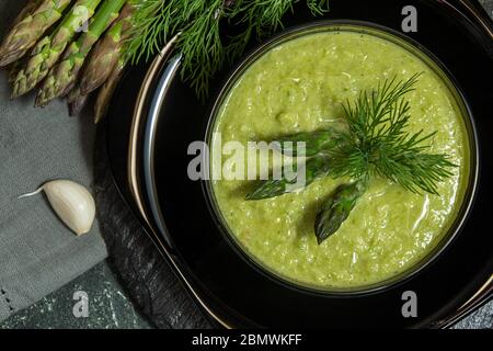 Cremige Spargelsuppe in Glasschüssel auf schwarzem Teller püriert. Draufsicht Stockfoto