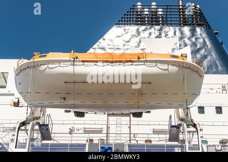 Rettungsboot mit orangefarbener Plane, die von einem Passagierschiff hängt Stockfoto