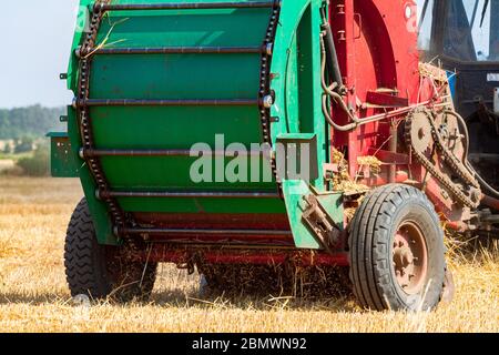 Ein Traktor mit einem gezogenen Ballen Maschine machen sammelt Strohrollen auf dem Feld und macht die Runde großen Ballen Stockfoto