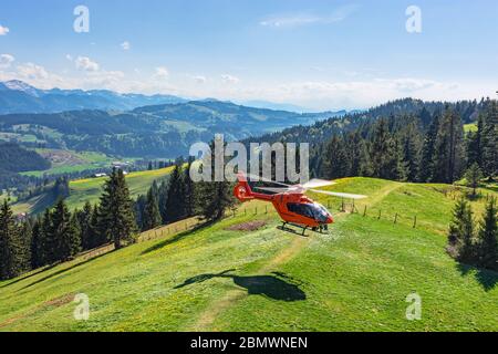 Roter Rettungshubschrauber der deutschen Lufttrettung landet auf einem grünen Hügel. Allgäu, Bayern, Deutschland Stockfoto