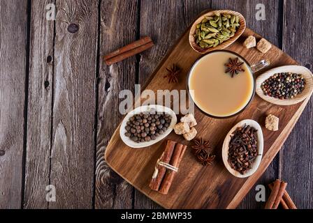 Traditionelles indisches Getränk - Masala Tee mit Gewürzen. Zimt, Kardamom, Anis, Zucker, Nelken, Pfeffer auf dunklem Holzhintergrund. Kopierbereich. Flaches Lay. Stockfoto