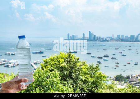 Hand halten kaltes Wasser und Meer mit vielen Booten in Pattaya in Thailand. Stockfoto
