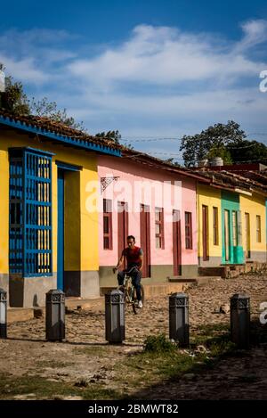 Mann Fahrrad fahren i eine typische Kopfsteinpflaster Straße mit bunten Häusern in der Kolonialzeit Zentrum der Stadt, Trinidad, Kuba Stockfoto
