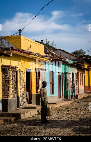 Mann, der in einer typischen Kopfsteinpflaster-Straße mit bunten Häusern im Kolonialzeitzentrum der Stadt, Trinidad, Kuba, steht Stockfoto