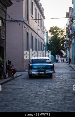 Oldtimer fahren durch eine stimmungsvolle Straße mit Kopfsteinpflaster in der Altstadt, Havanna Vieja, Havanna, Kuba Stockfoto