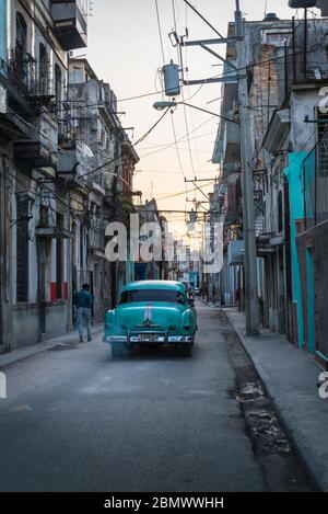 Oldtimer fahren durch eine stimmungsvolle Straße mit Kopfsteinpflaster in der Altstadt, Havanna Vieja, Havanna, Kuba Stockfoto