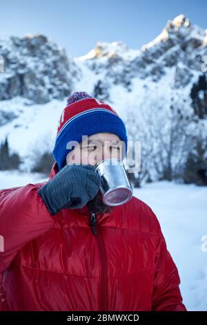 Reisende Mann mit Bart ist das Trinken von Tee oder Kaffee aus dem Becher in den Bergen im Winter. Camping Mountain Konzept. Stockfoto