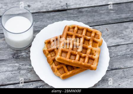 Blick von oben auf den Teller mit belgischen oder wiener Waffeln mit einem Glas frischer Milch auf einem rustikalen Holztisch Stockfoto