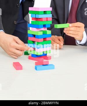 Bunte Blöcke ragen auf einem weißen Schreibtisch. Zwei Männer spielen ein Brettspiel. Geschäftsstrategie, Risiko, Baukonzept Stockfoto