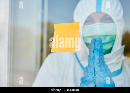 Gelbe Post-it-Notiz an Tür oder Fenster der Klinik mit Arzt in Schutzkleidung während der Coronavirus-Epidemie Stockfoto