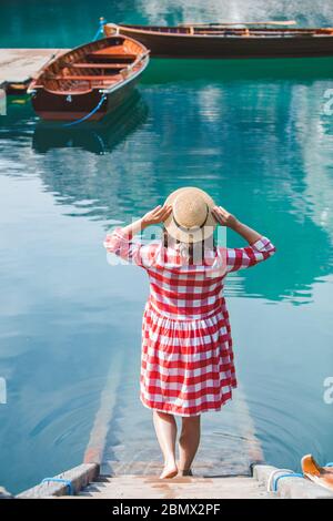 Junge Frau in roter Sonnenkleid, die über Treppen zum Seewasser geht Stockfoto