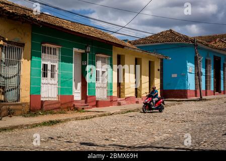 Motorradfahrer in einer typischen Kopfsteinpflaster Straße mit bunten Häusern im Kolonialzeitzentrum der Stadt, Trinidad, Kuba Stockfoto