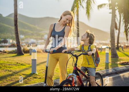 Aktiver Schuljunge und seine Mutter fahren ein Fahrrad mit Rucksack an sonnigen Tag. Fröhliches Kinderradeln auf dem Weg zur Schule. Sichere Art und Weise für Kinder im Freien zur Schule Stockfoto