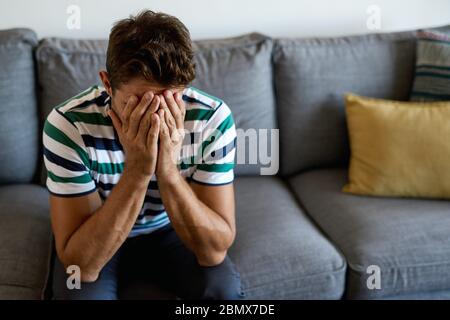 Junger Mann sitzt auf seinem Sofa und sieht verstört aus Stockfoto