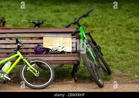 Fahrräder, die sich während der Blockade des Covid-19 in London, 10. Mai 2020, an einer Parkbank mit einem Coronavirus-Anweisungsschild in Clapham Common lehnen Stockfoto