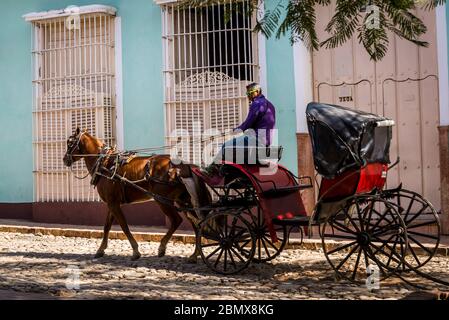 Mit dem Pferd und Wagen fahren Sie durch eine typische Kopfsteinpflaster-Straße mit bunten Häusern im Kolonialzeitzentrum der Stadt, Trinidad, Kuba Stockfoto