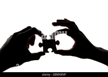 Silhouette einer Hand hält ein Puzzle-Teil auf einem weißen Hintergrund Stockfoto