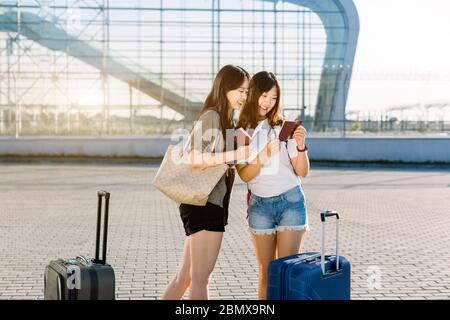 Zwei schöne glückliche junge asiatische Frauen in lässiger Kleidung, überprüfen ihre Pässe und Flugtickets, während in der Nähe des modernen Flughafen-Gate mit Stockfoto