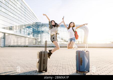 Reise- und Urlaubskonzept. Zwei junge asiatische Mädchen mit Koffern, Pässen und Flugtickets, sind von ihrer Reise begeistert, springen auf und Stockfoto