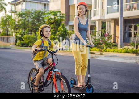 Aktive Schule Kind Junge und seine Mutter in Sicherheitshelm Reiten ein Fahrrad mit Rucksack an sonnigen Tag. Fröhliches Kinderradeln auf dem Weg zur Schule. Sichere Art und Weise für Kinder Stockfoto