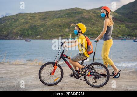 Aktive Schulkind und seine Mutter in medizinischen Maske und Schutzhelm Reiten ein Fahrrad mit Rucksack an sonnigen Tag. Fröhliches Kinderradeln auf dem Weg zur Schule. Sie Stockfoto