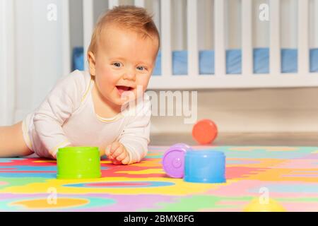 Schöne lachende Baby Kleinkind Junge kriechen auf dem Boden der Kindergarten Grabbing Spielzeug in der Nähe Krippe Stockfoto