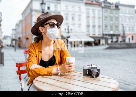 Junge Frau in Gesichtsmaske allein auf der Terrasse des Cafés sitzend. Konzept der sozialen Distanzierung und neue soziale Regeln nach der Coronavirus-Pandemie. Stockfoto