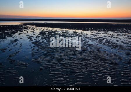 Atlantischer Sonnenuntergang in Frankreich. Die Flut ist niedrig, der Sand ist überall gestreift. Das Licht ist schön, seine Farben auch. Diese Landschaft ist friedlich. Stockfoto