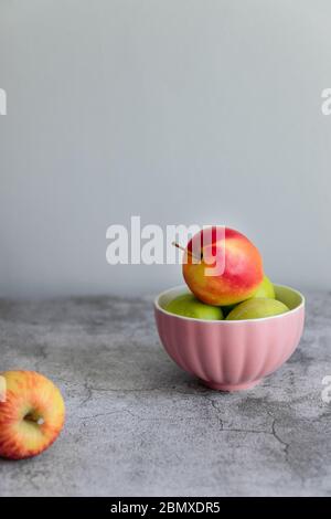 Grün rot Bio gesunde Äpfel in rosa Schale auf grauem Brett, vertikal Foto Stockfoto