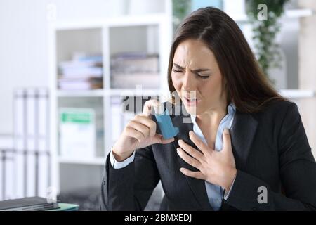 Leitende Frau hält Inhalator mit Asthmaanfall erstickend sitzt auf einem Schreibtisch im Büro Stockfoto