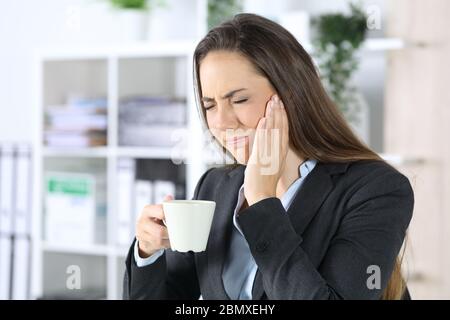 Exekutive Frau in Schmerzen mit Zahnschmerzen hält Kaffeetasse im Büro sitzen Stockfoto