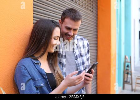 Glückliches Paar sprechen über smart phone Inhalt in einem bunten Straße Stockfoto