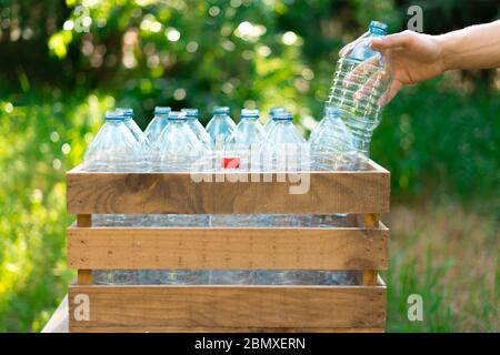 Wiederverwendung von Kunststoffflaschen Recycling-Konzept. Man's Hand, eine Plastikflasche in einer recycelten Holzkiste mit Kunststoff-Wasserflaschen ohne Kappe mit Stockfoto