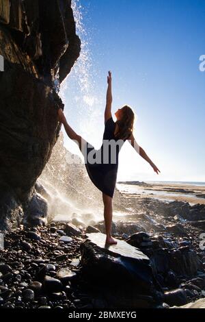 Eine junge Tänzerin macht Dehnungsübungen unter einem Wasserfall Stockfoto