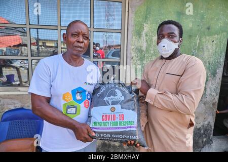 Ein Freiwilliger übergibt einem Mann während der Covid-19-Sperre in Lagos, Nigeria, eine Lebensmittelverpackung. Stockfoto